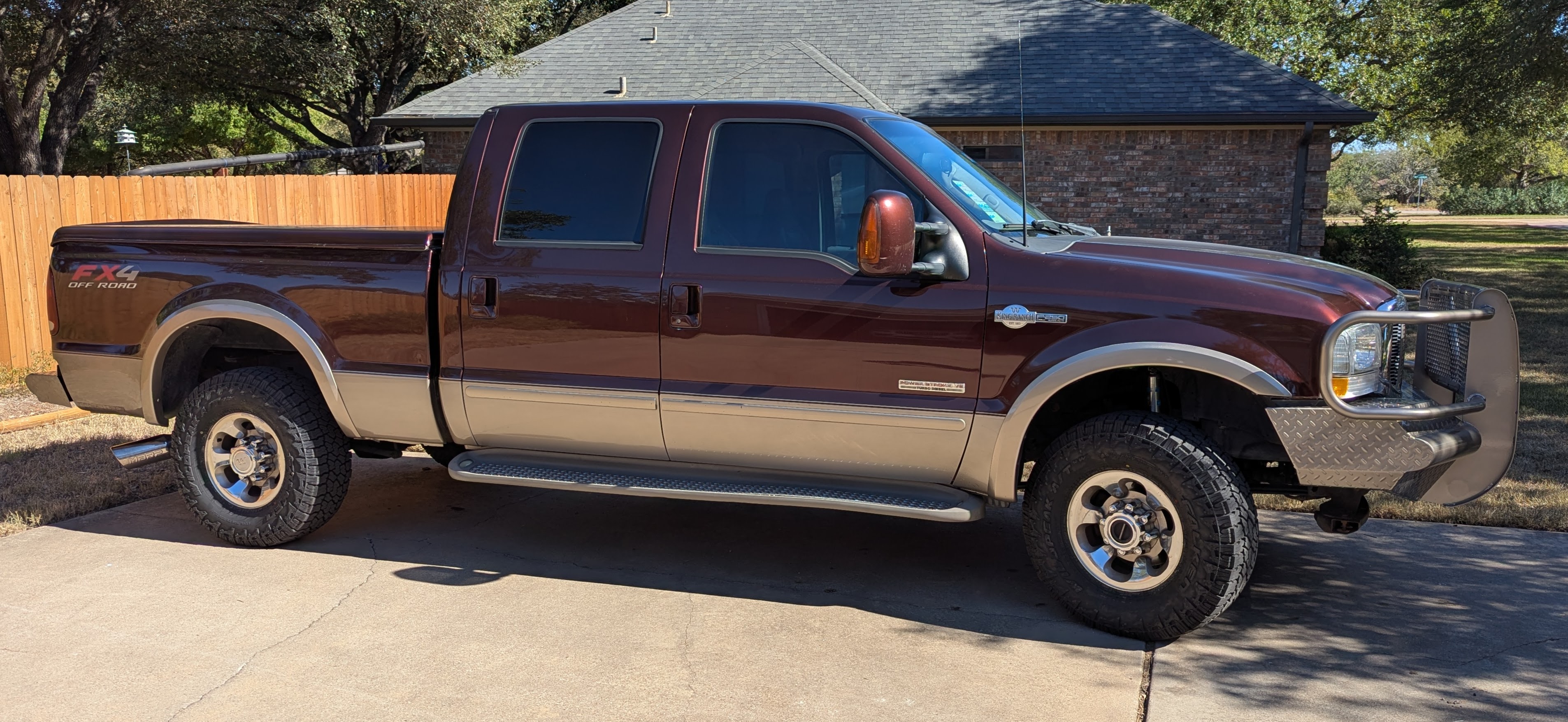 A 2003 Ford F-250 with a maroon paint job parked in a camping park in front of a travel trailer.